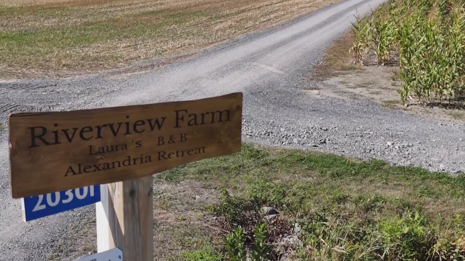 Load video: Video showcasing the exterior of Laura&#39;s B&amp;B featuring items like a blacony, beautifully landscaped entryway, flags of Canada and France, and a farmland view sourrounded by the lush trees of Glengarry.