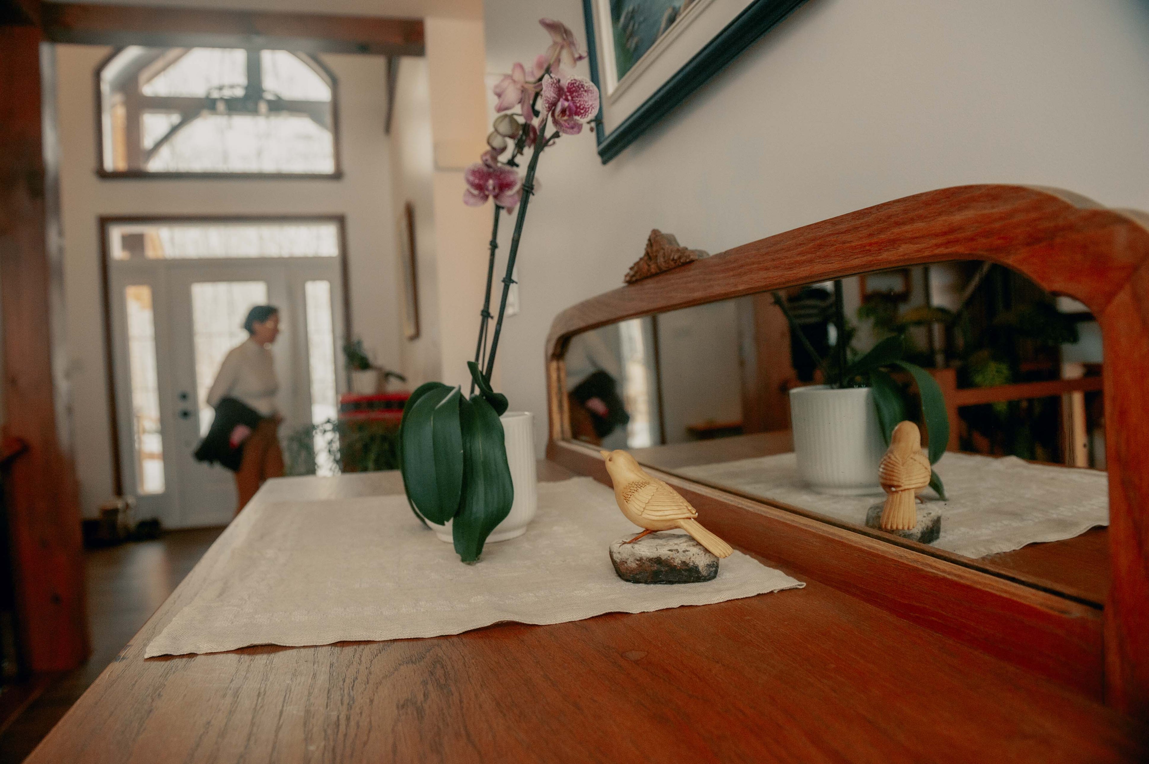 Table setting with a vase of flowers, bread, and a mirror reflecting a room.